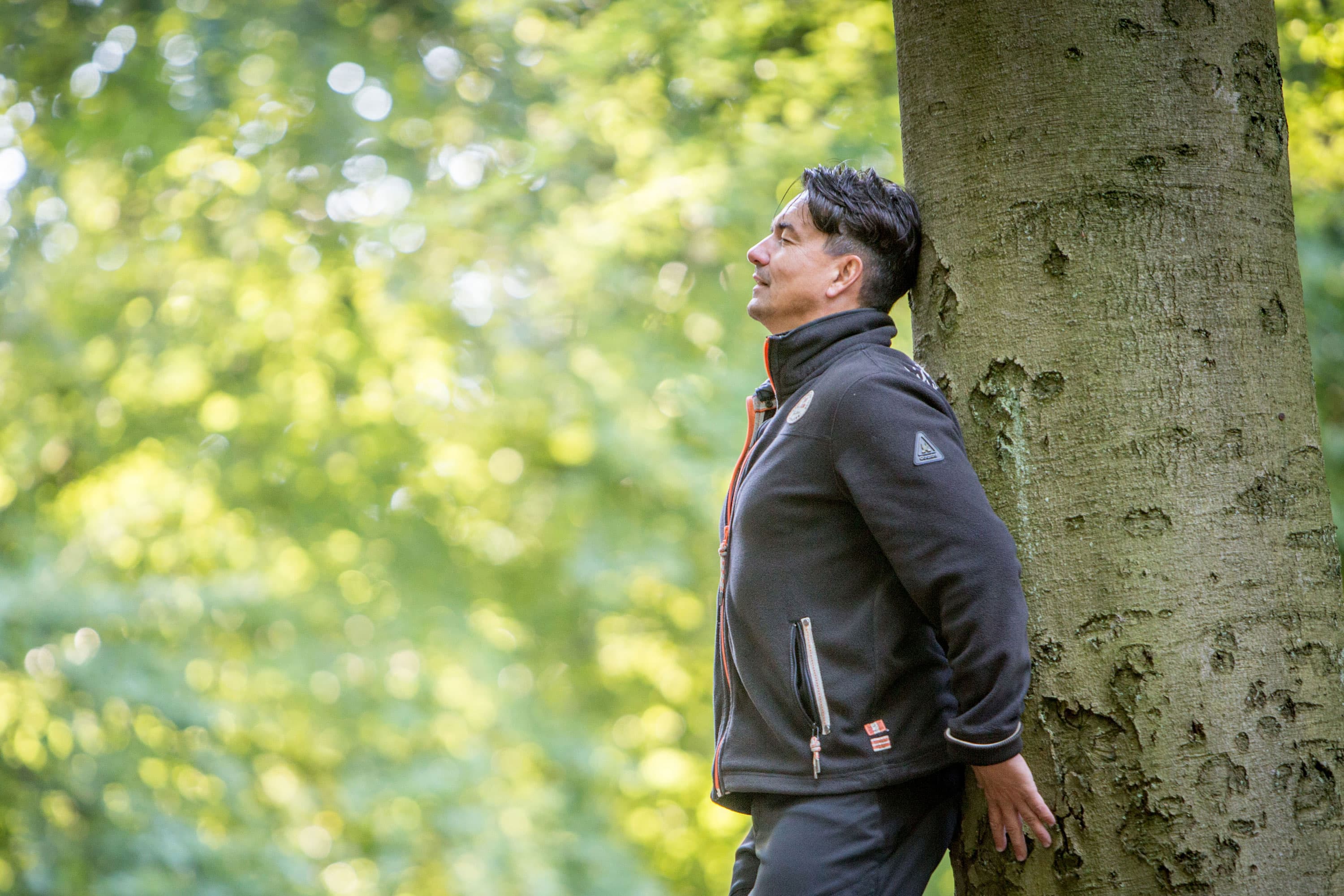 Mann lehnt sich mit geschlossenen Augen an einem Baum im Wald.