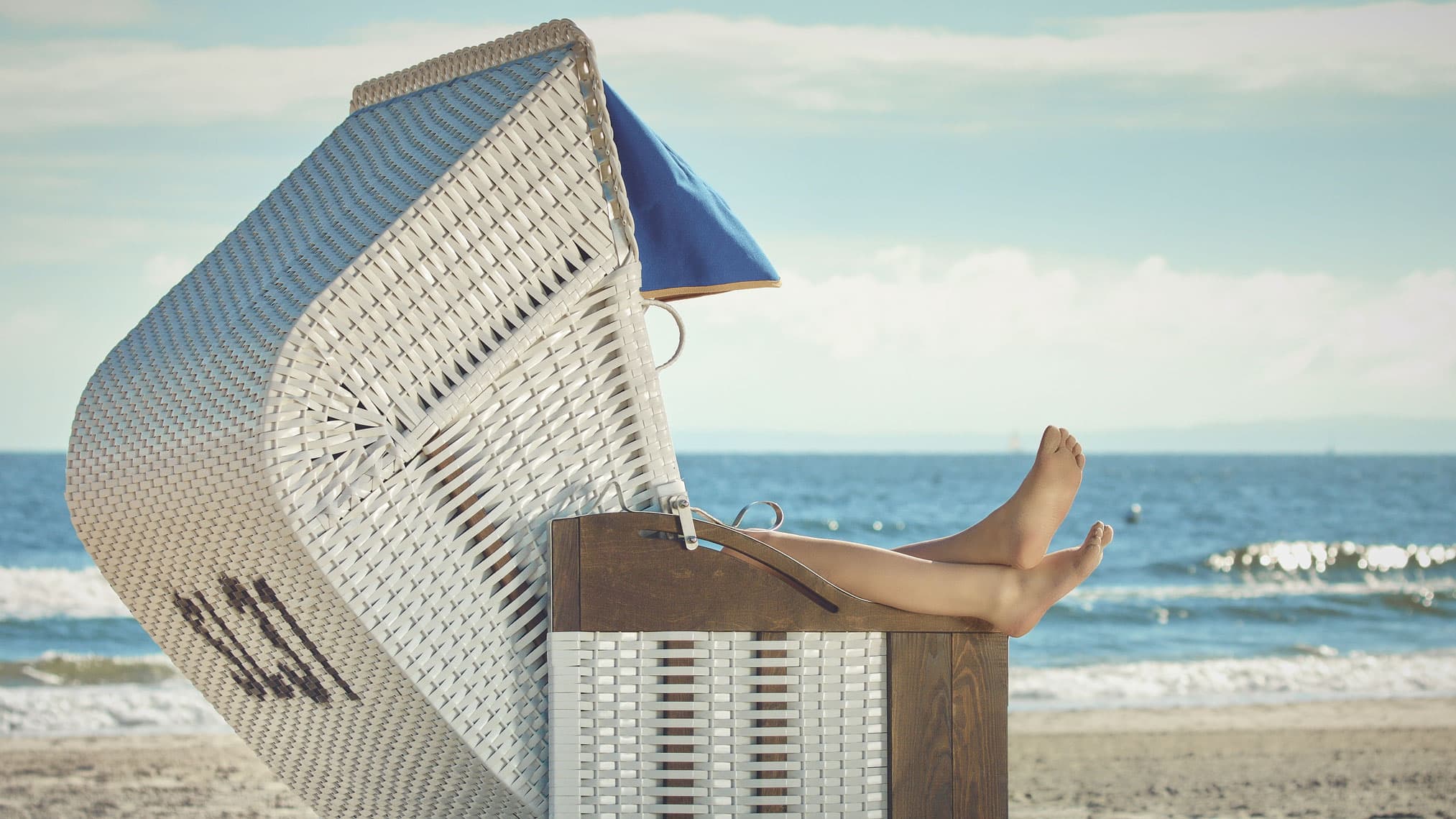 Person sonnt sich im Strandkorb am Strand. 
