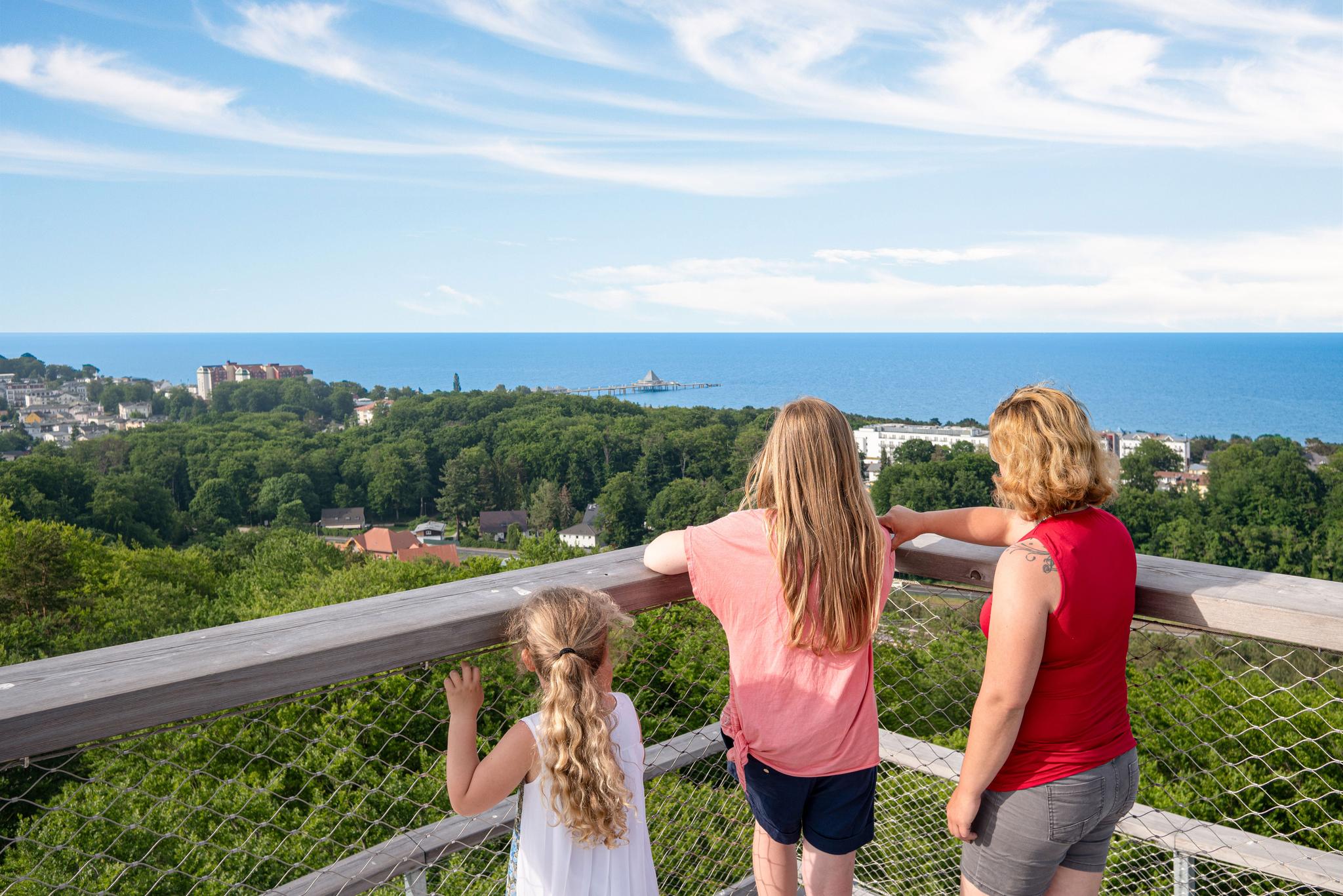 Drei Personen auf dem Aussichtsturm blicken auf die Ostsee.