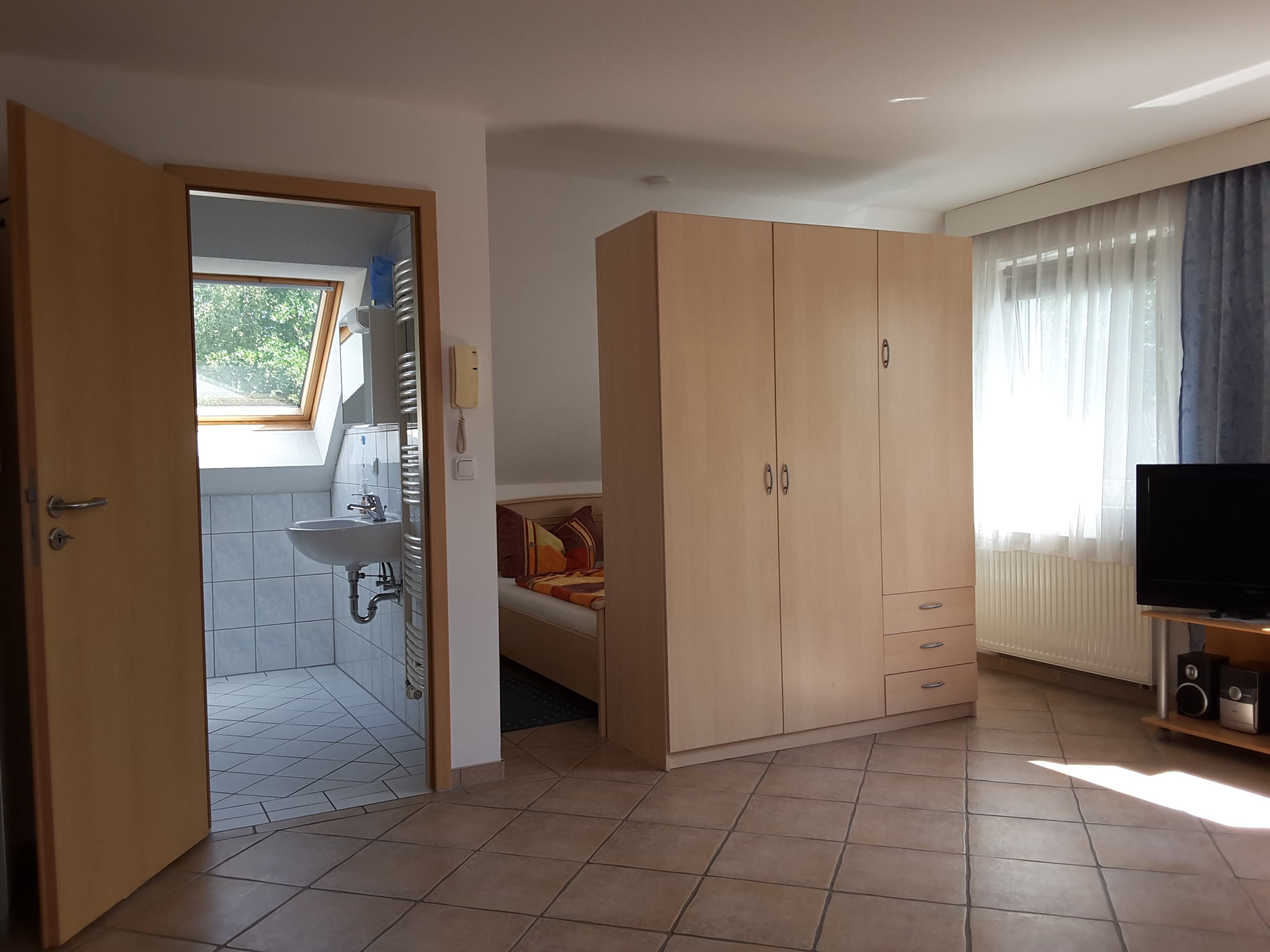 Raum mit Schrank in der Mitte und einer Tür am linken Bildrand. 