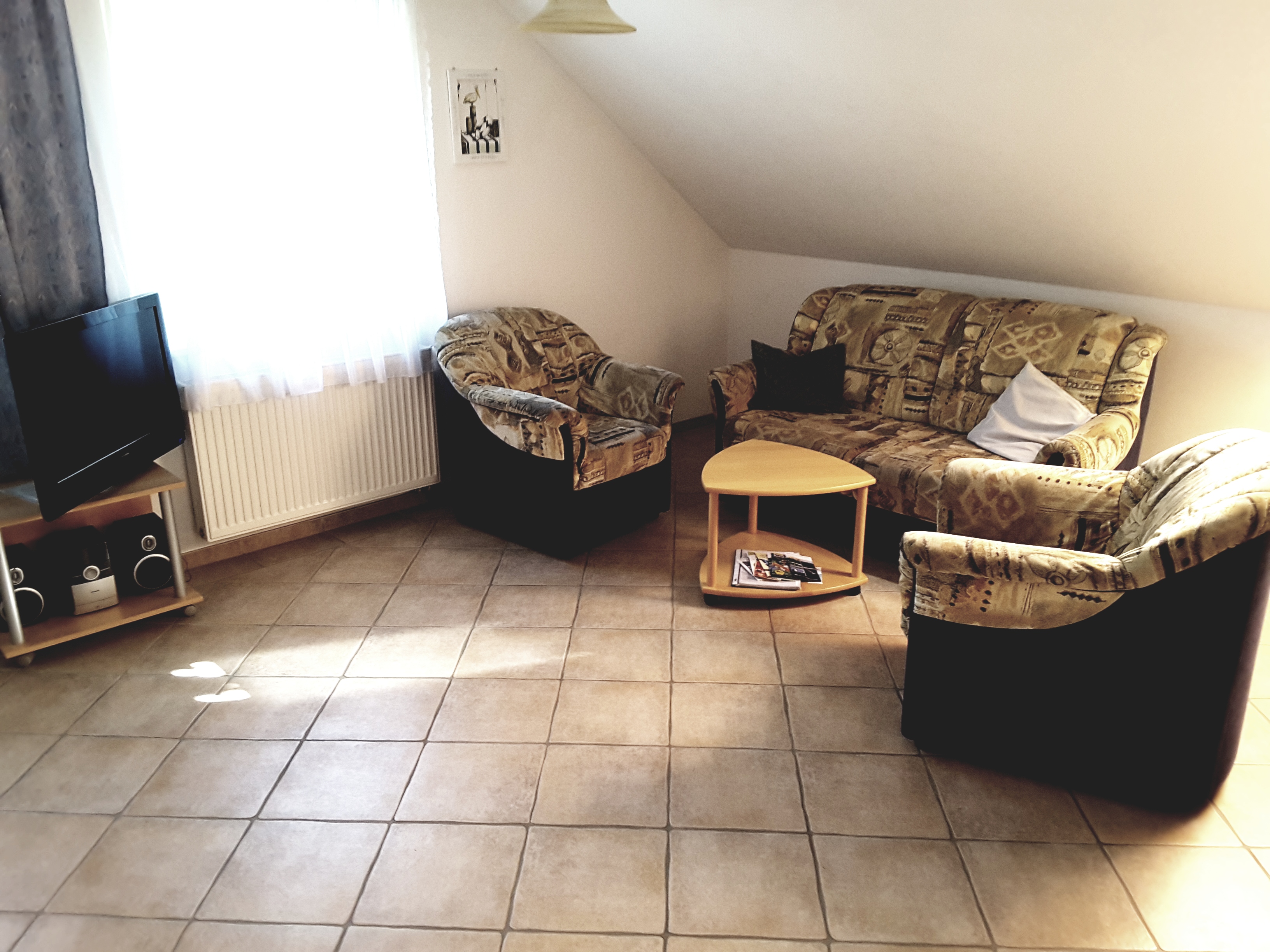 Wohnzimmer mit einer Sitzecke unter der Dachschrägen und einem Fernseher.