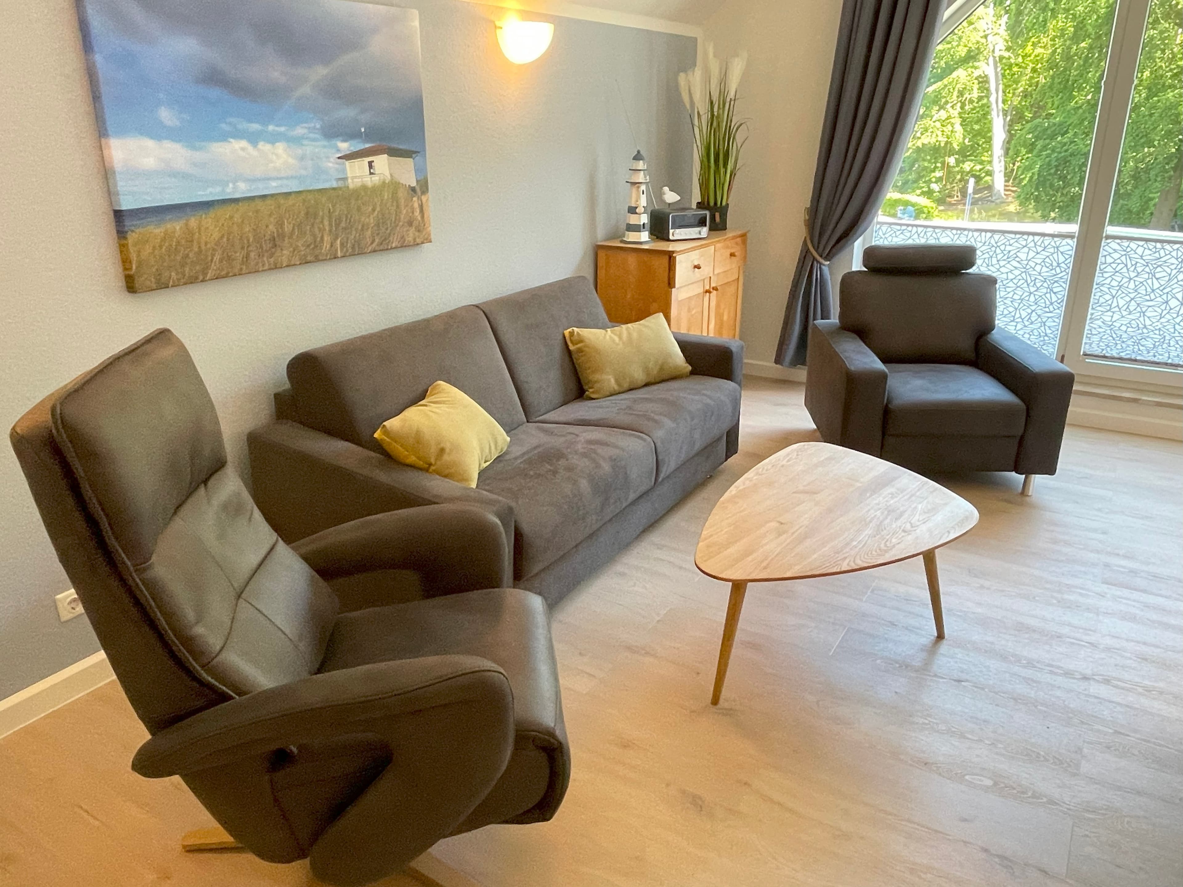 Wohnzimmer  mit grauer Couch, Holztisch und schwarzen Sesseln.