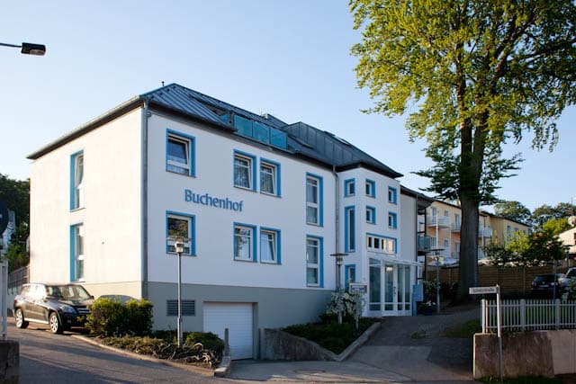 Das Foto zeigt eine Außenansicht des Haus Buchenhof in Heringsdorf. Das Haus ist dreistöckig, weiß bemalt und hat ein blaues Dach.