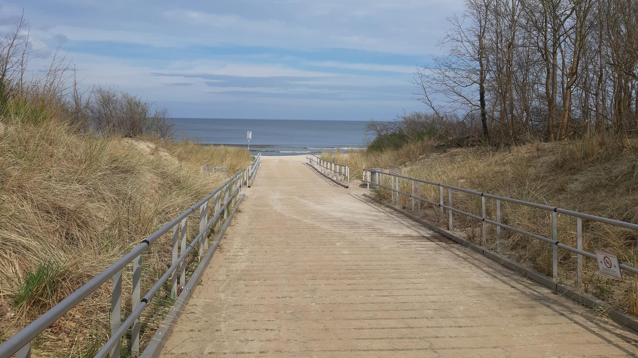 Breiter Holzweg mit beidseitigem Metallgeländer führt zum Strand.