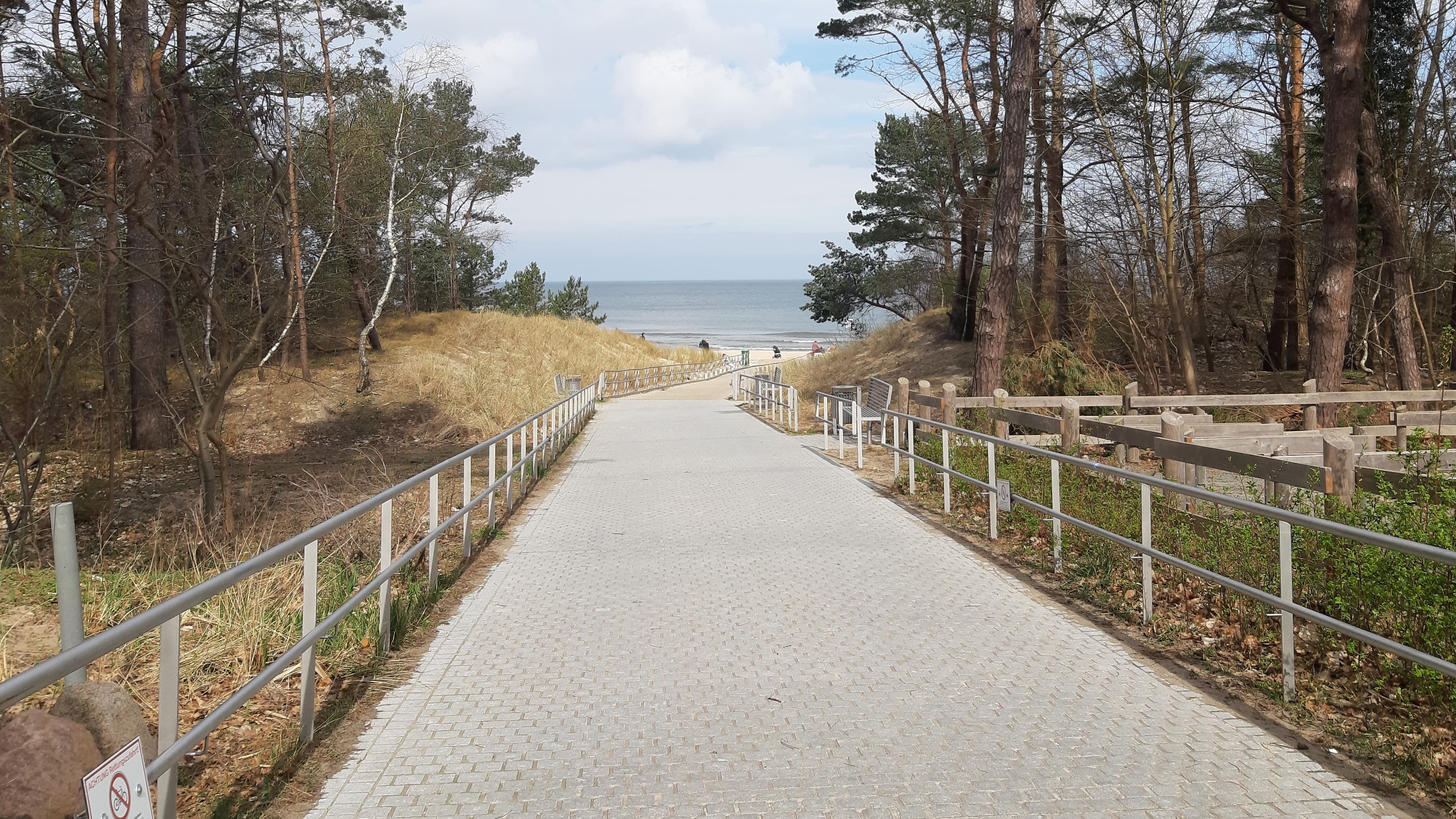 Breiter gepflasterter Weg mit Metallgeländer führt bis zum Strand.