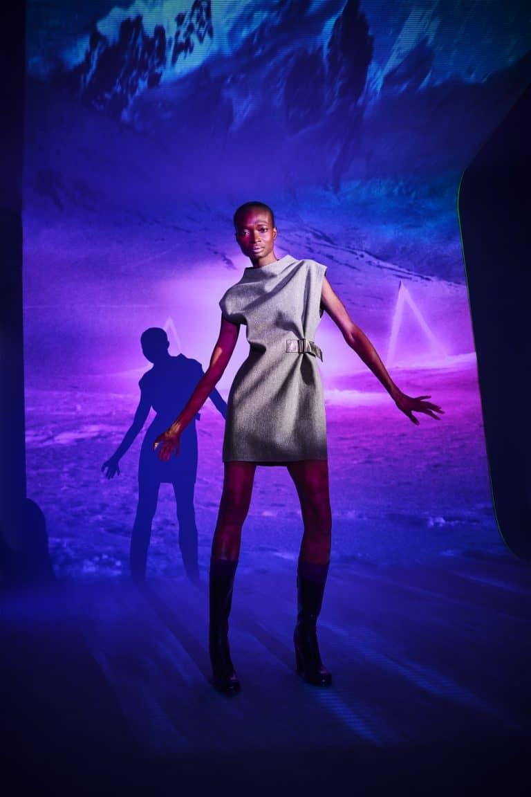 Model posiert mit einem grauen Kleid von dem Modelabel Alpin Lodge vor einer Lichtreflexion eines Gletchers und wirft einen Schatten auf die Wand hinter sich.