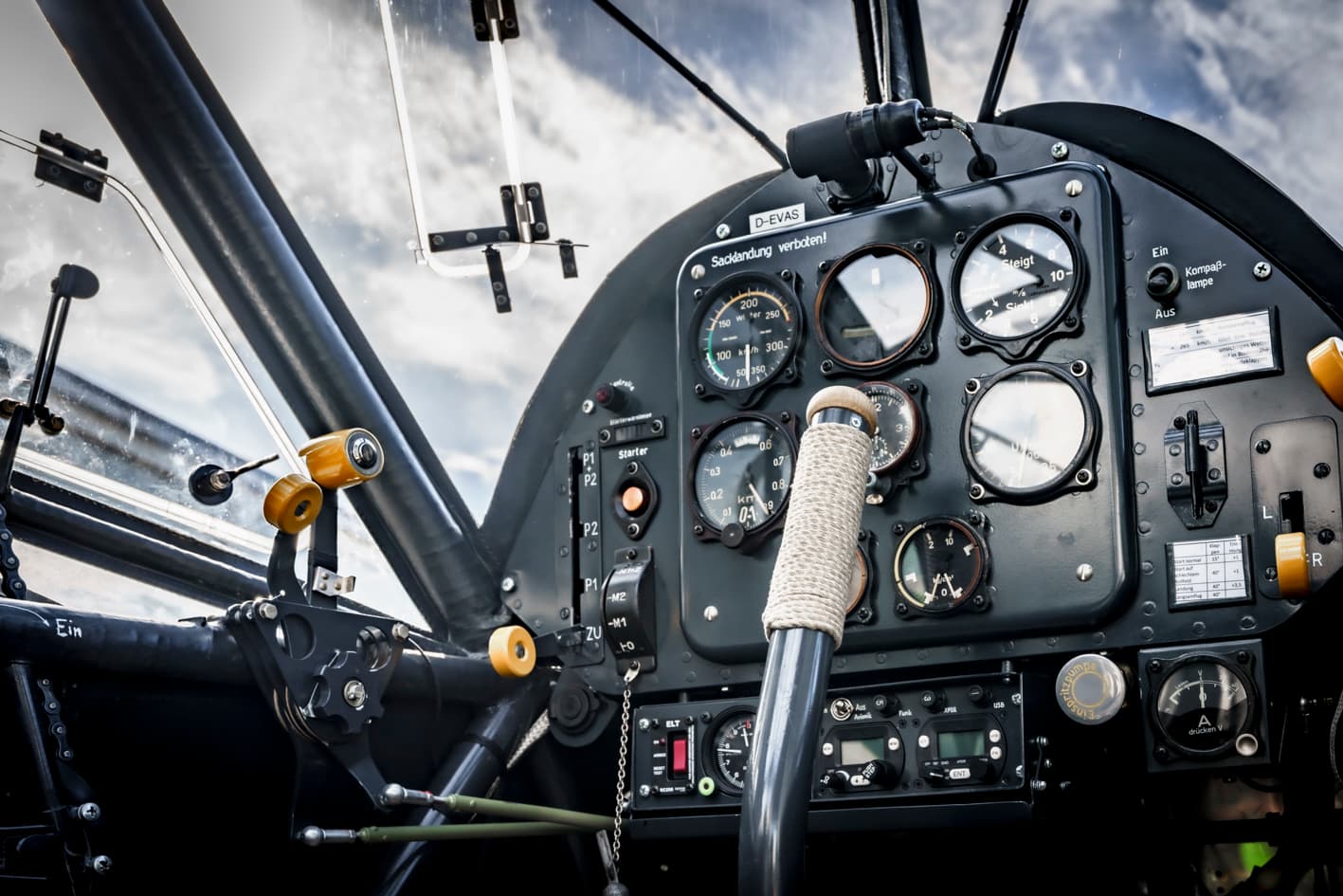 Man sieht ein Cockpit eines Oldtimer-Flugzeugs aus der Innenperspektive. Das Flugzeug befindet sich in der Luft, da man die Wolken sieht.