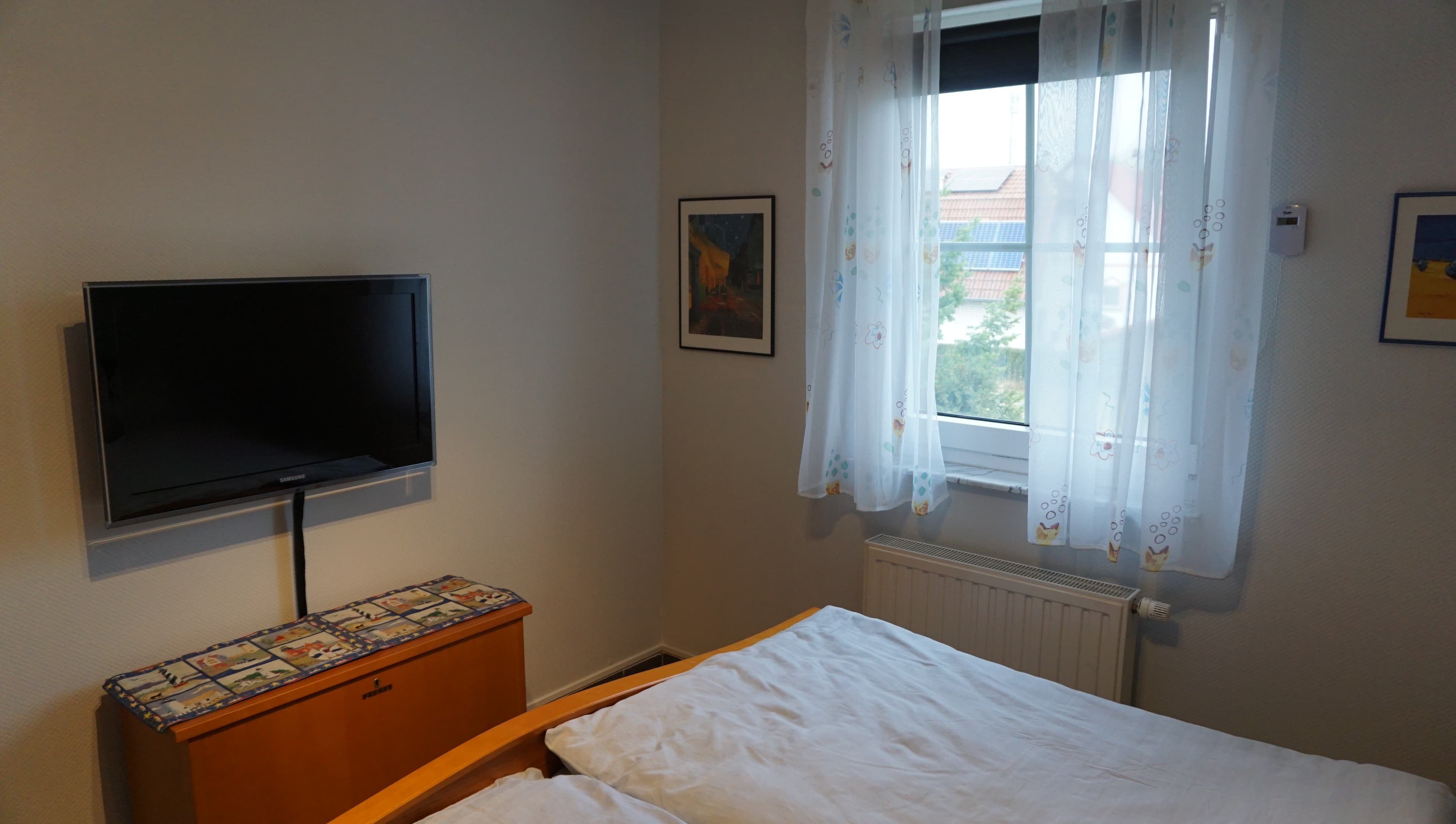 Schlafzimmer mit TV-Gerät und Fenster mit Gardinen und Verdunklungsrollo