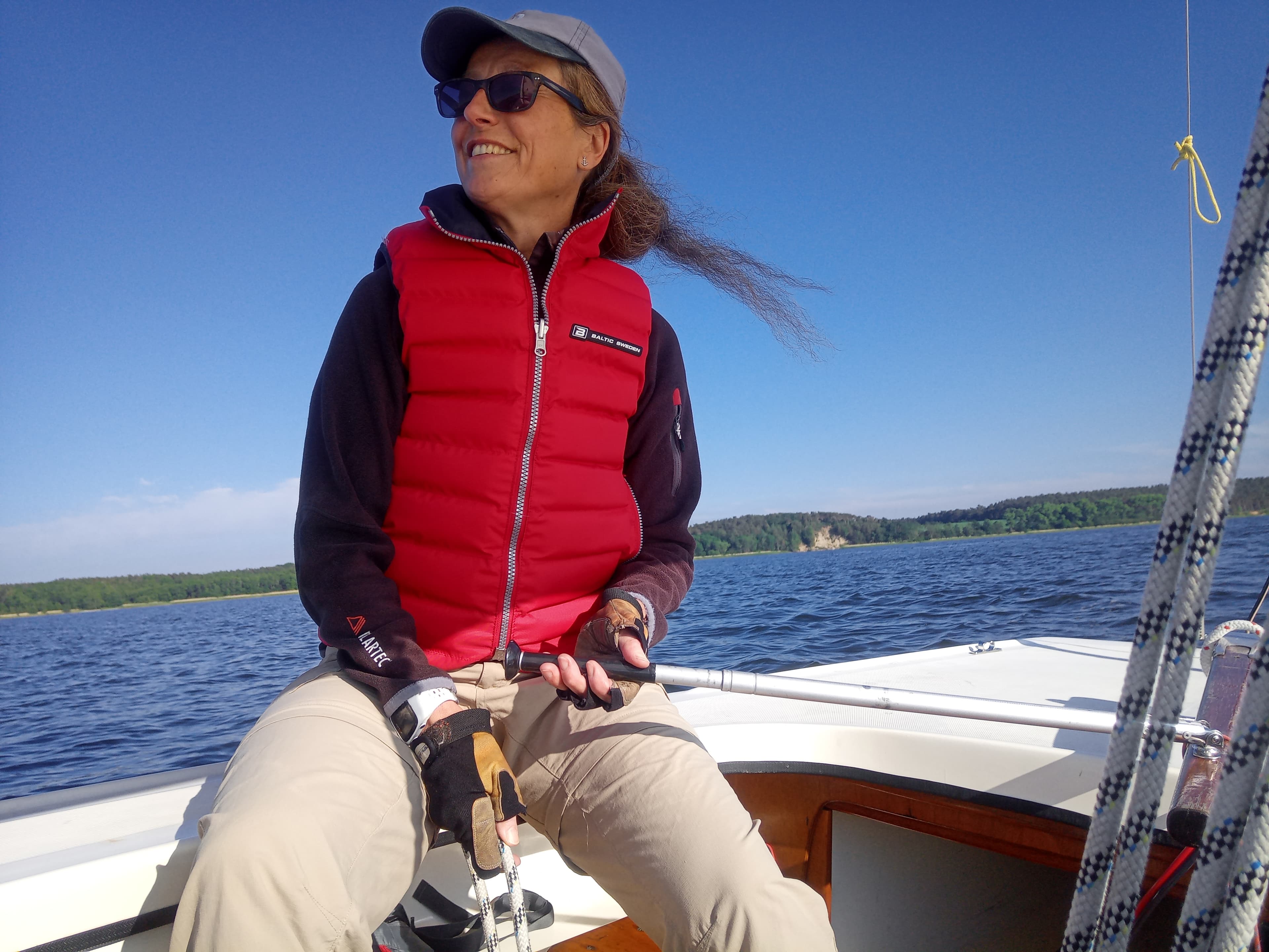 Frau mit roter Weste auf einem Segelboot unterwegs auf dem Wasser, strahelnd blauer Himmel