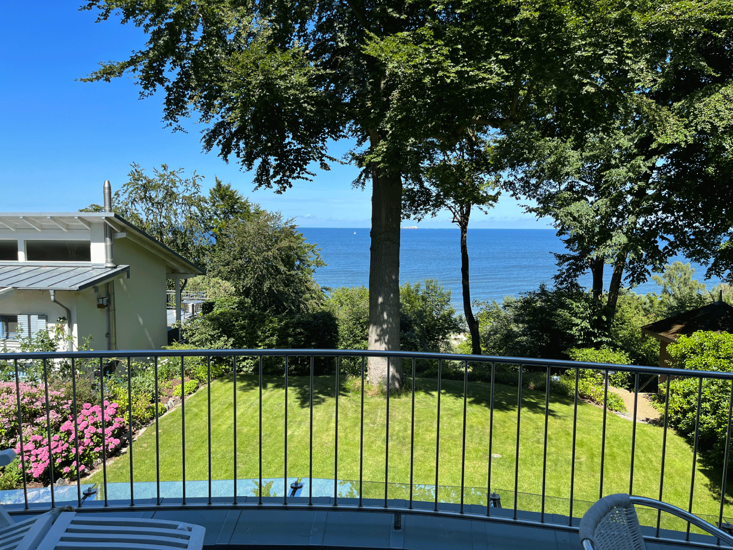 Ausblick von einem Balkon, auf eine grüne Wiese, einem Baum und dahinter das Meer