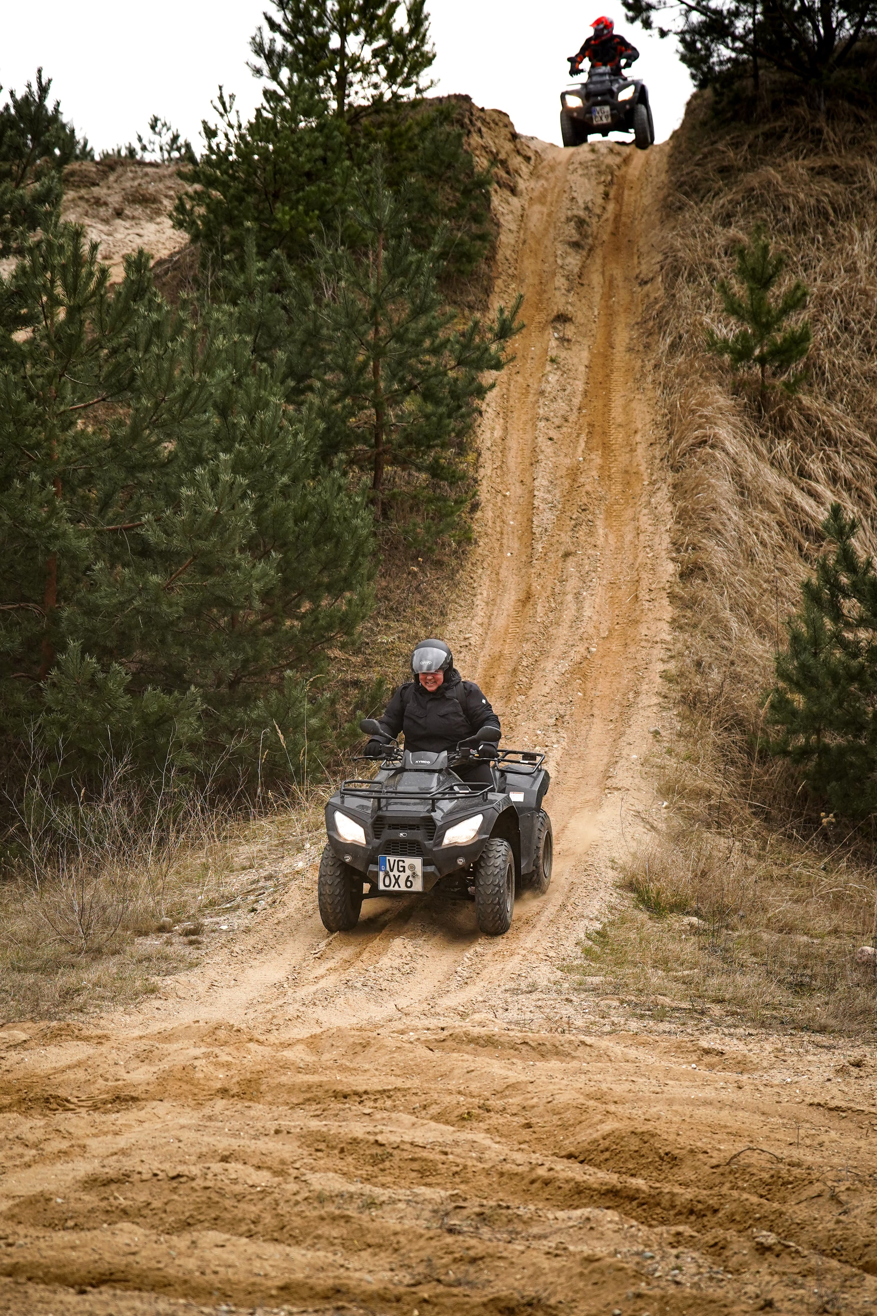 zwei Quad Fahrer fahren einen steilen Abhang hinunter, sie sind in einer Kiesgrube unterwegs
