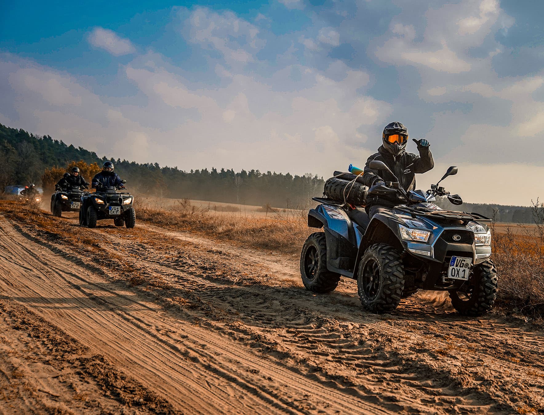 Man sieht 4 Personen auf Quads, die über einen Sandweg fahren. Der Himmel ist blau, es ist herrliches Wetter.