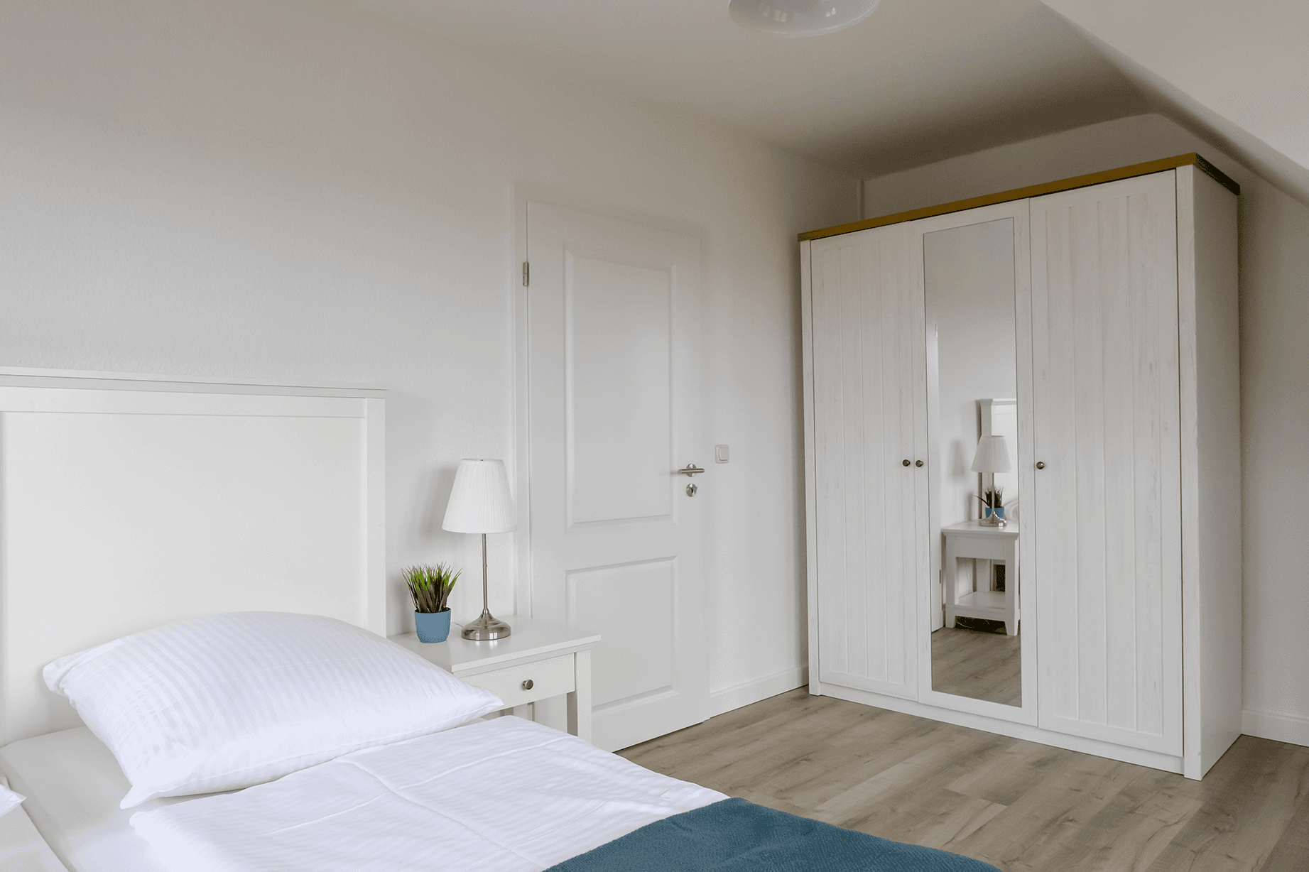 Schlafzimmer: helles weißes Bett und großer weißer Schrank