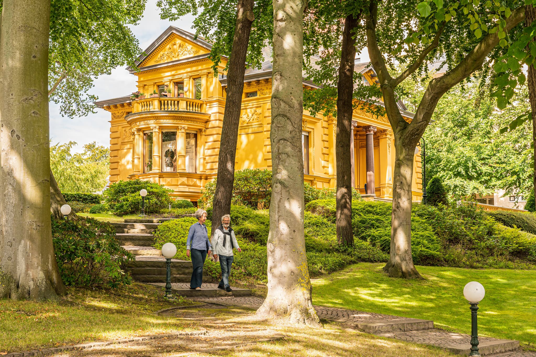 Pärchen auf einem Weg vor einer gelben Bädervilla