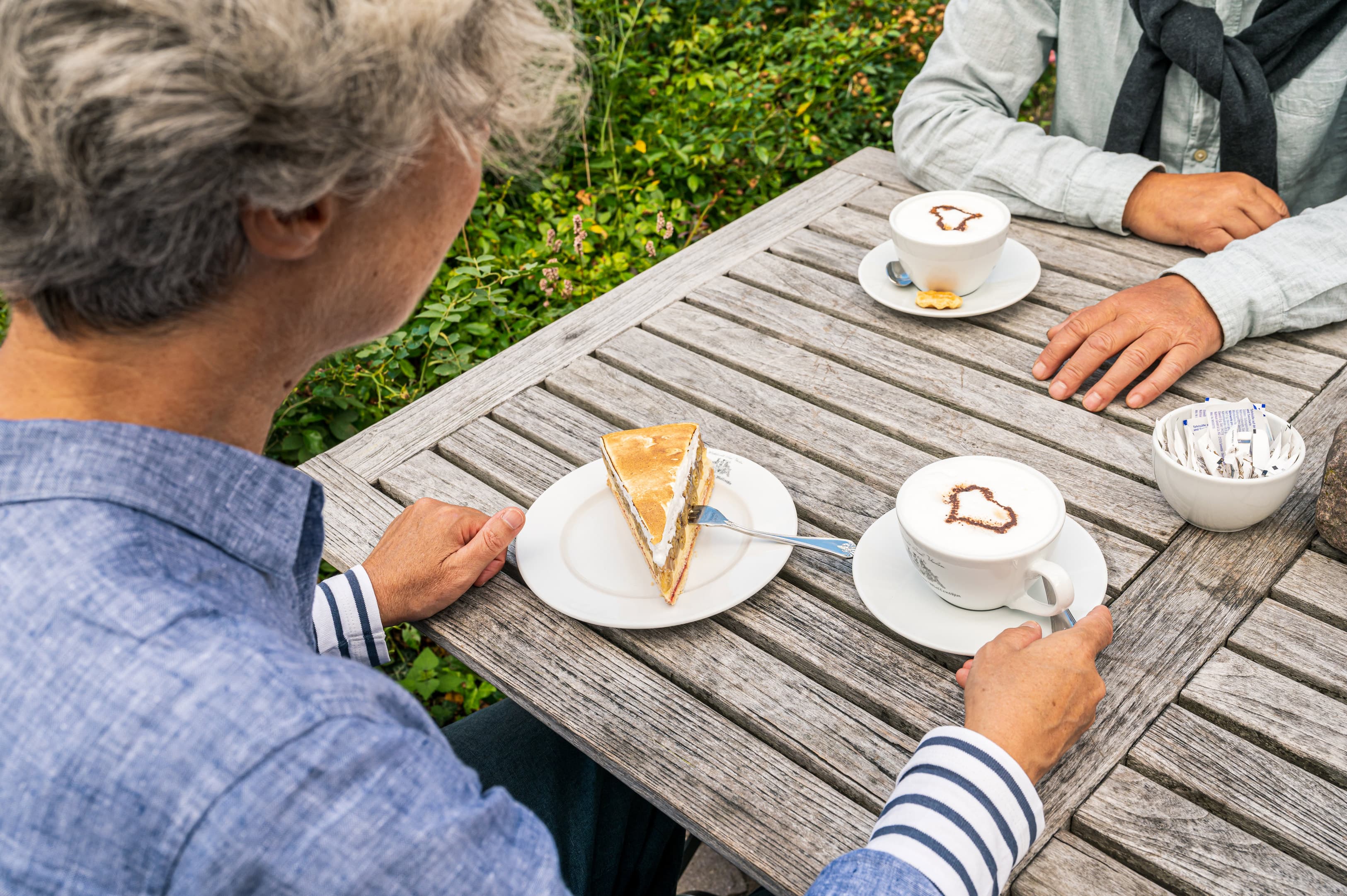 zwei Personen an einem gedeckten Holztisch mit Kaffee und Kuchen