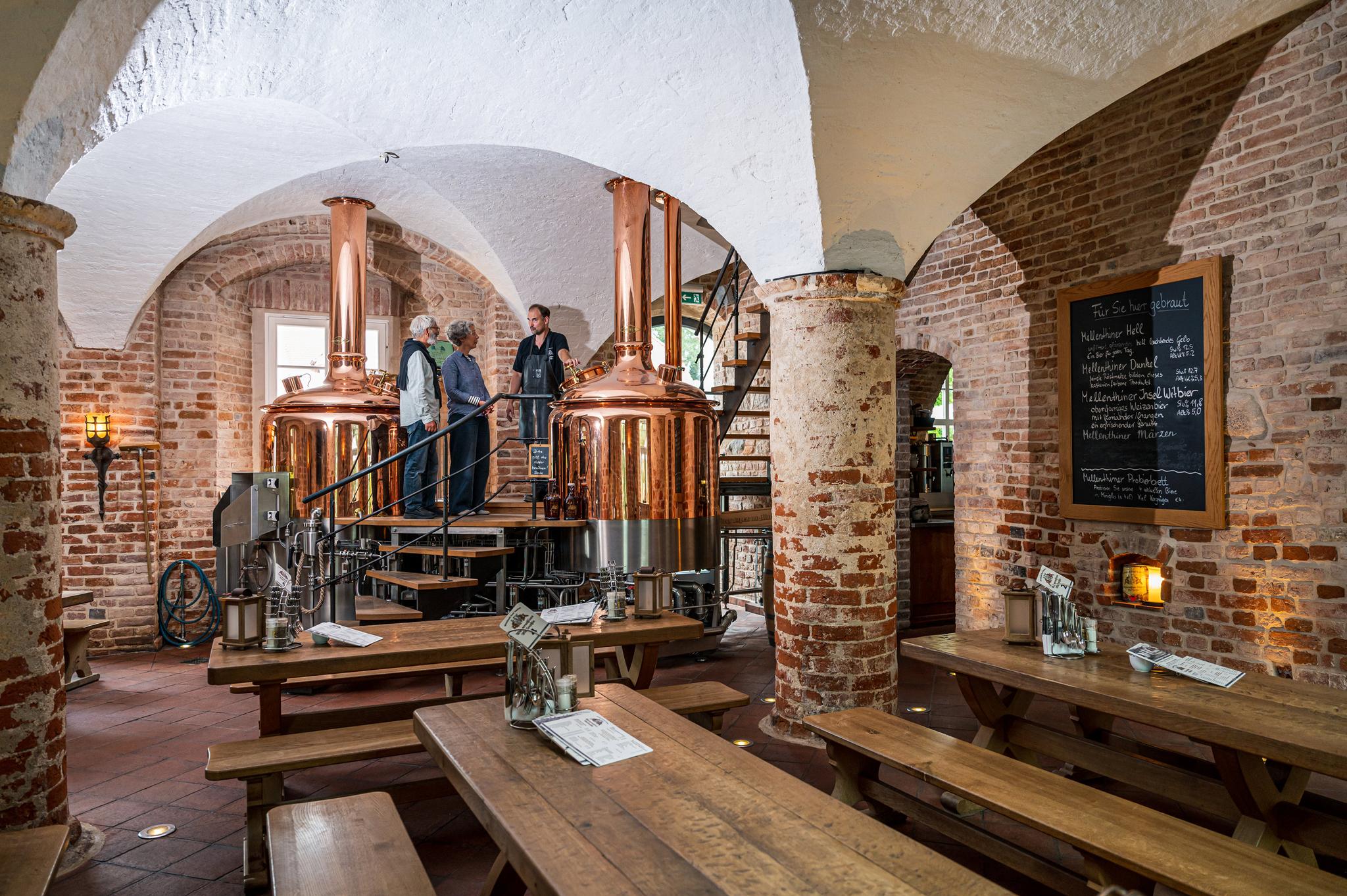 Drei Personen stehen vor den Braukesseln der Brauerei im Wasserschloss Mellenthin.