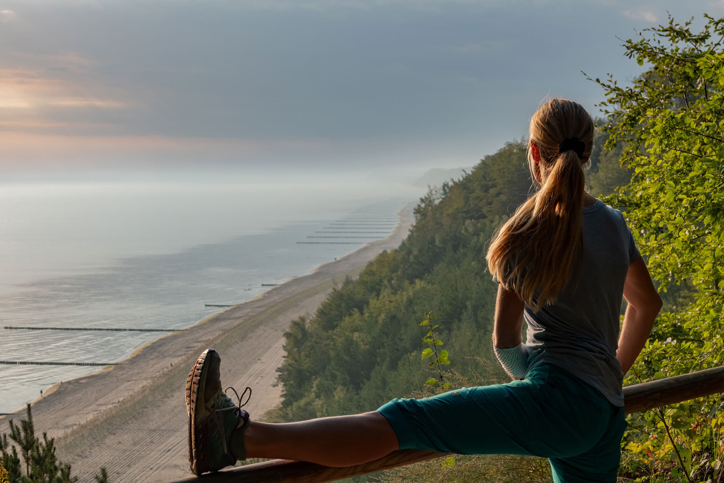 Frau dehnt sich an einem Geländer auf dem Streckelsberg und blickt auf die Ostsee.