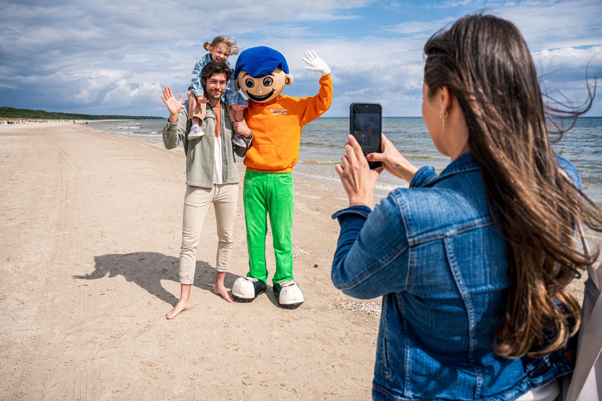 Frau fotografiert Familie mit Maskottchen am Strand von Karlshagen