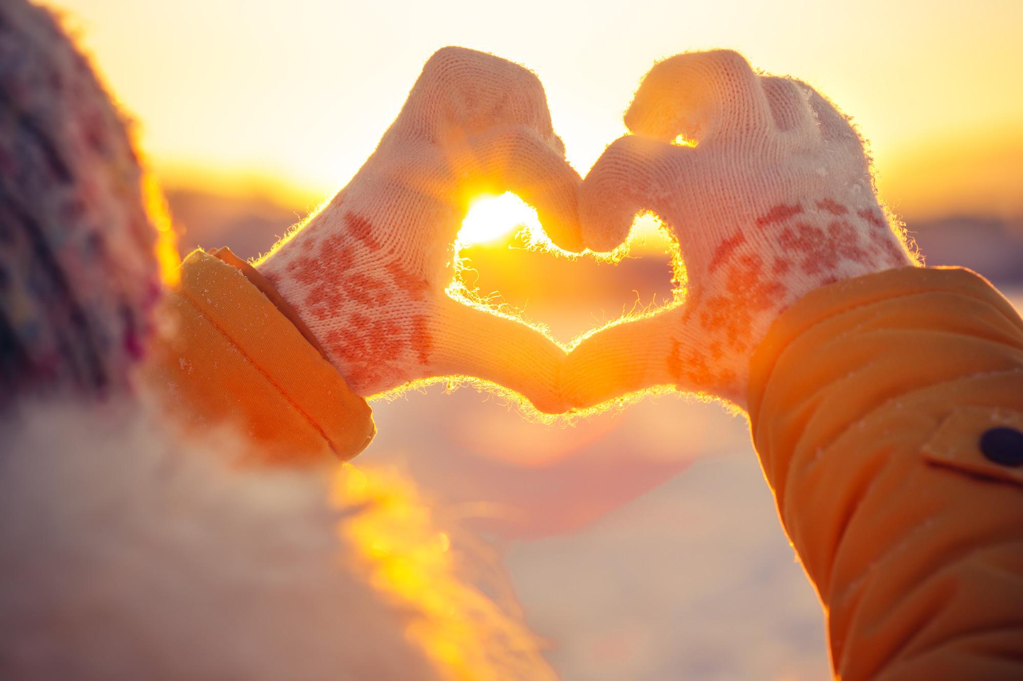 Person formt Herz mit Händen im Winter am Strand