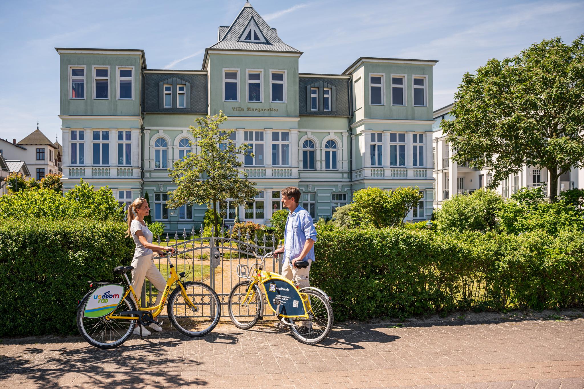 Pärchen steht mit Fahrrädern vor einer Bäderarchitektur-Villa.