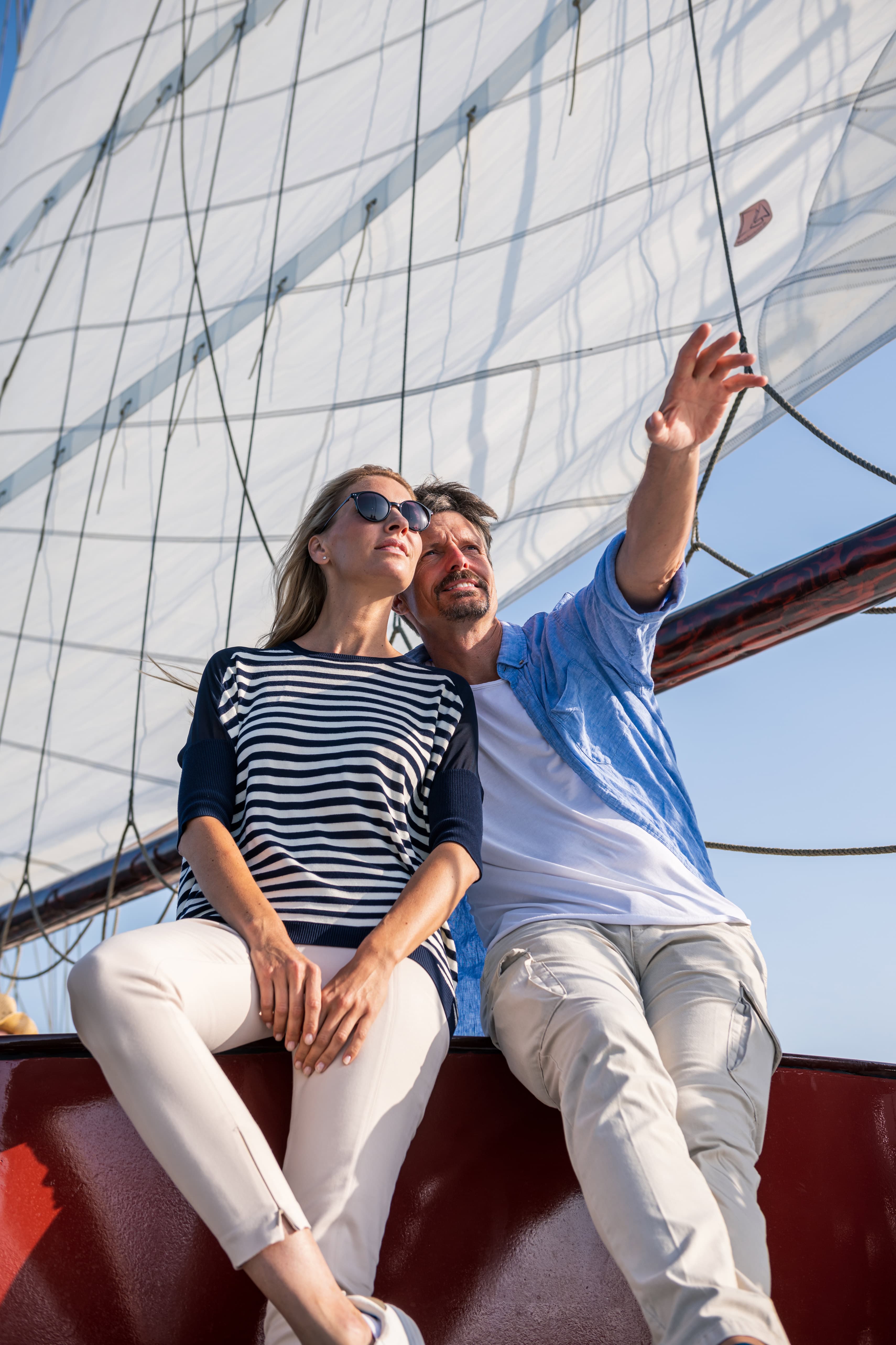Pärchen sitzt vor einem Segel auf einem Segelschiff.