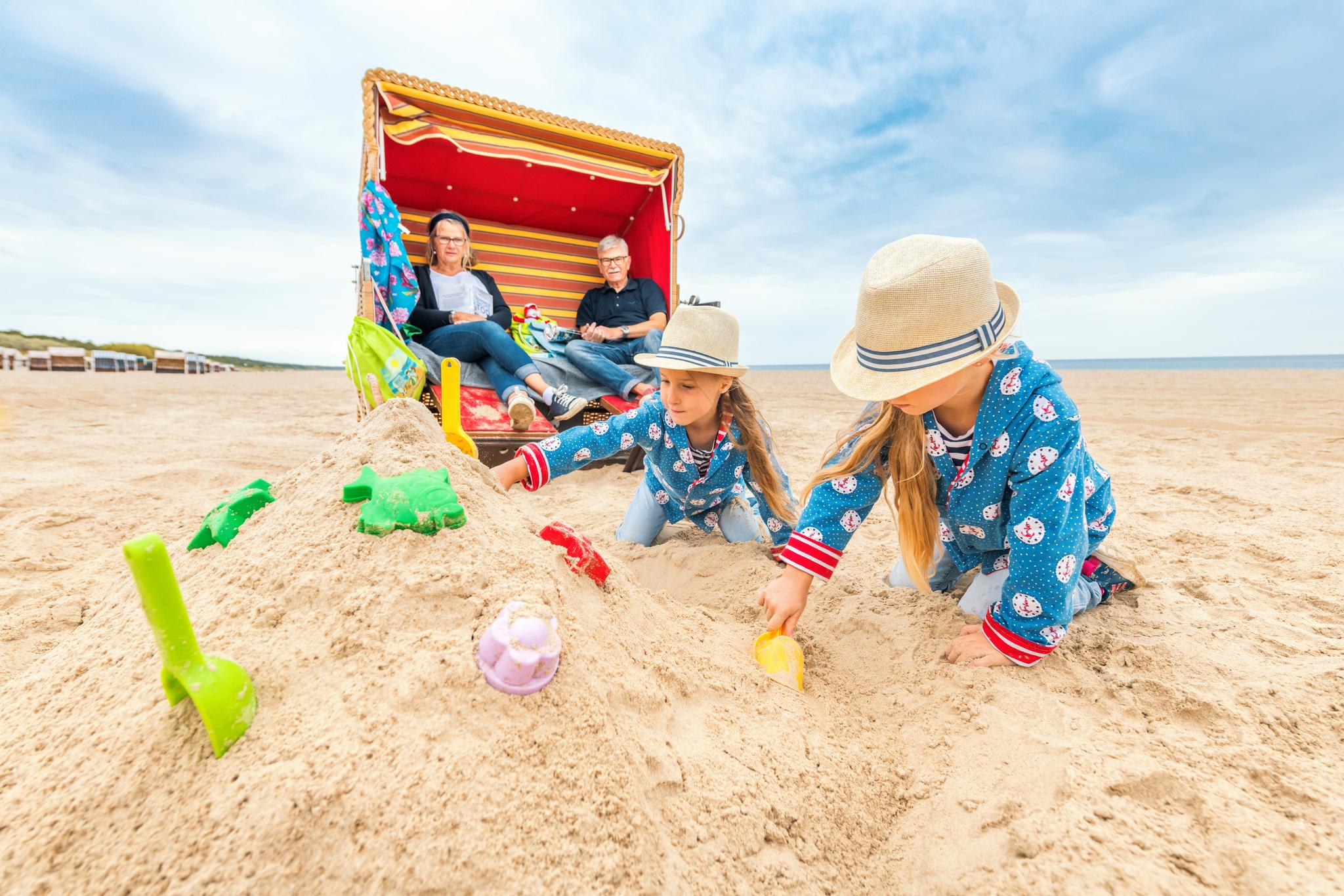 Kinder buddeln im Sand vor einem Strandkorb