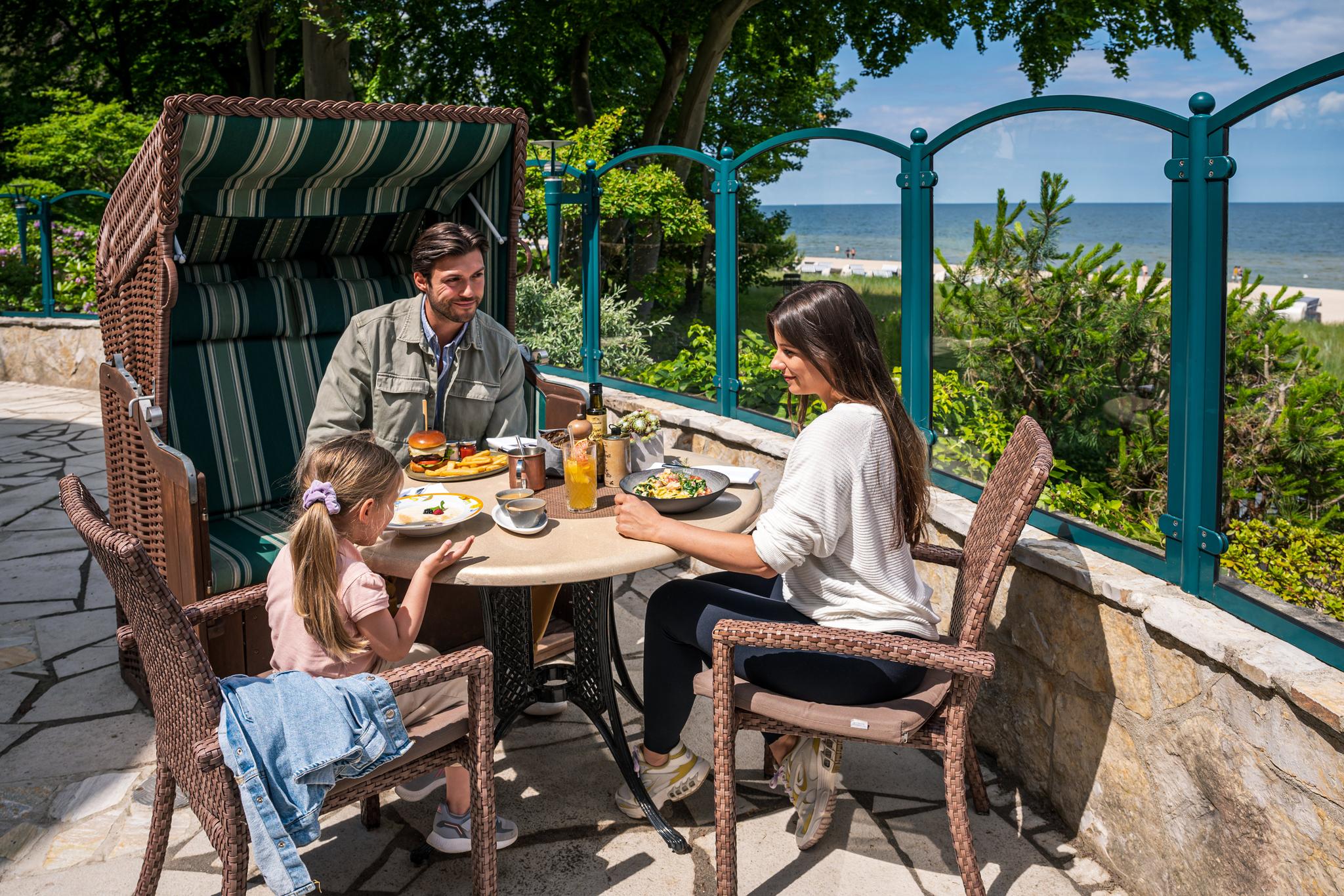 Familie sitzt an gedecktem Tisch auf Terrasse mit Ostseeblick.