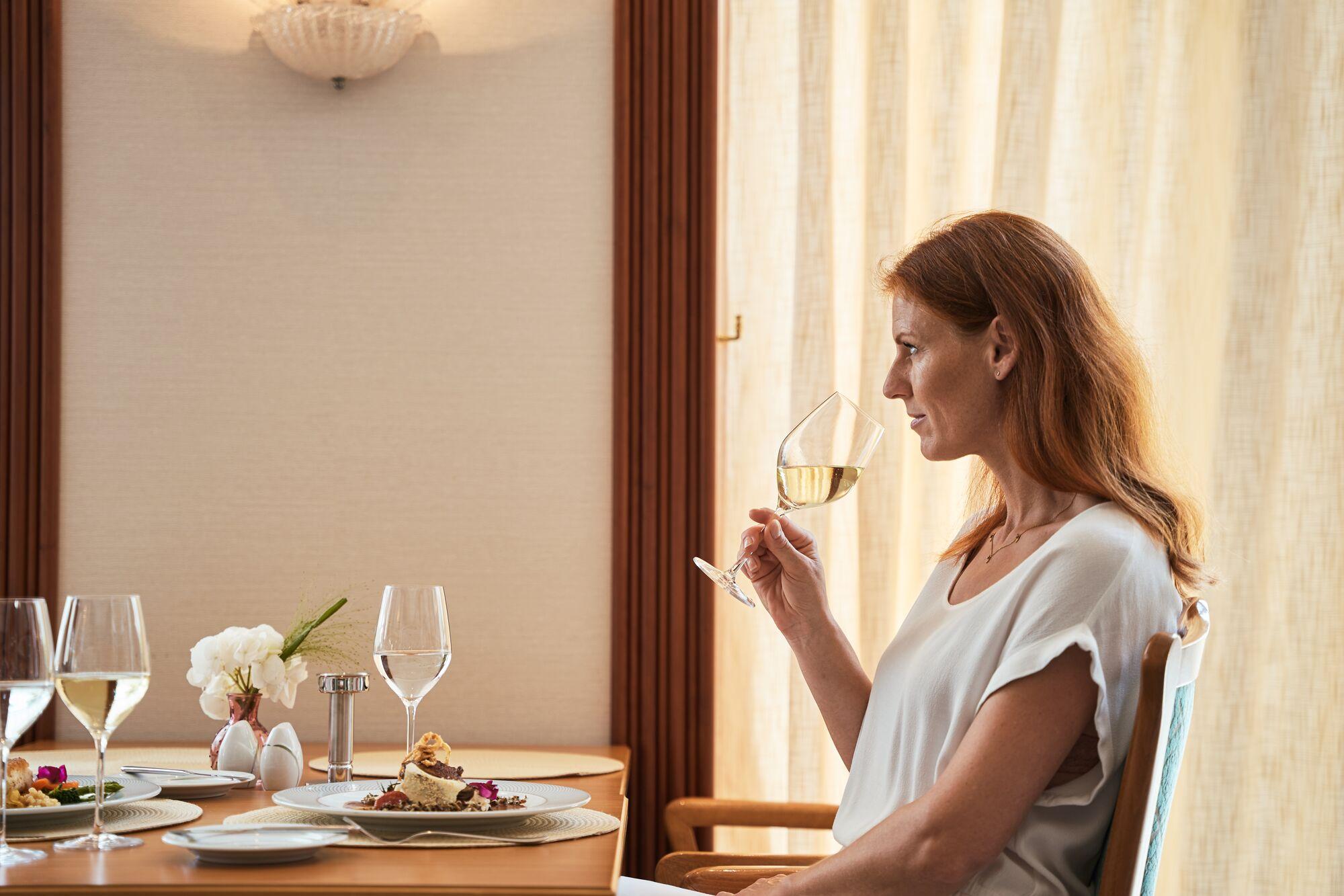 Frau sitzt an einem Esstisch mit Weinglas in der Hand