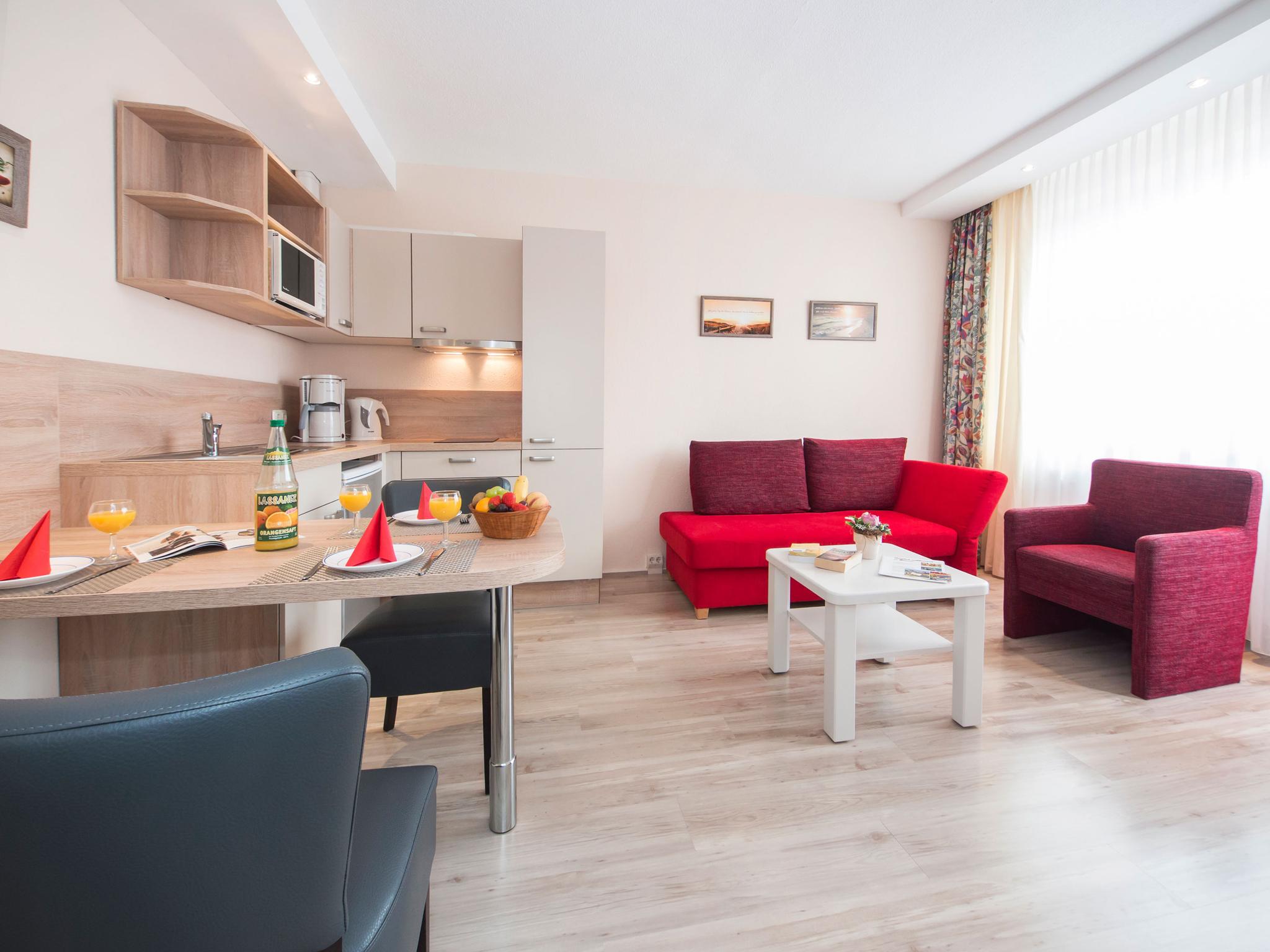 Wohnzimmer mit roten Möbeln kombiniert mit Küchenzeile in Holzoptik.