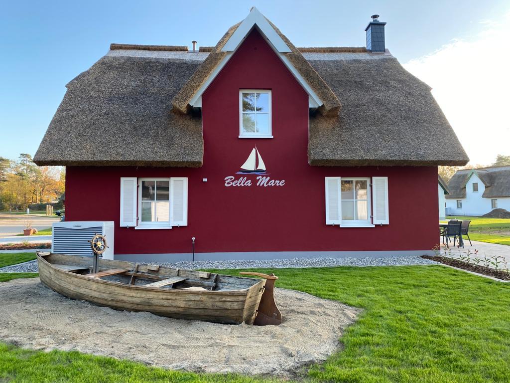 Rotes Ferienhaus mit Holzschiff im Sand davor