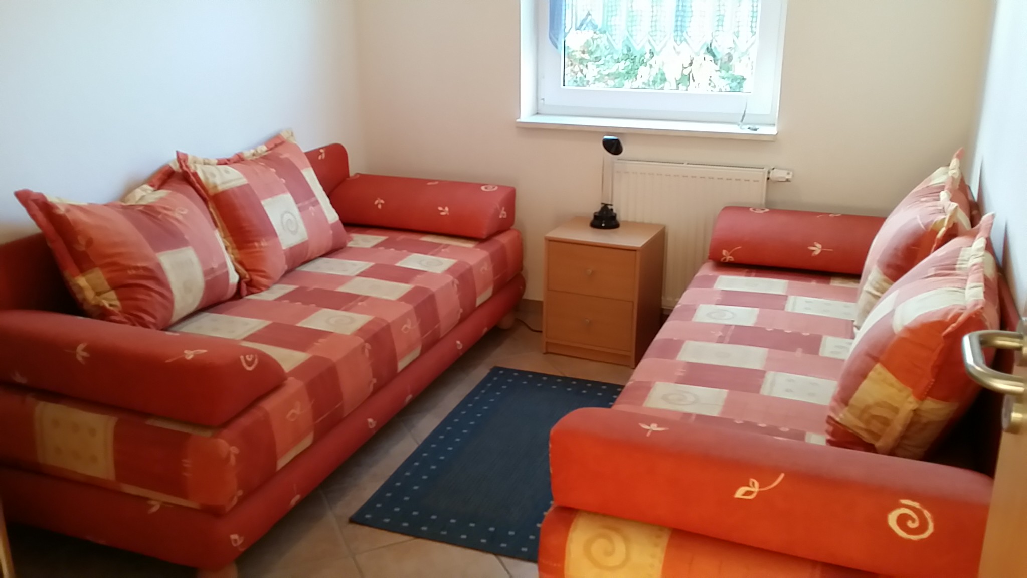 Zwei orange Sofas mit jeweils zwei Sitzplätzen. Beide stehen sich in einem schmalen Raum gegenüber.