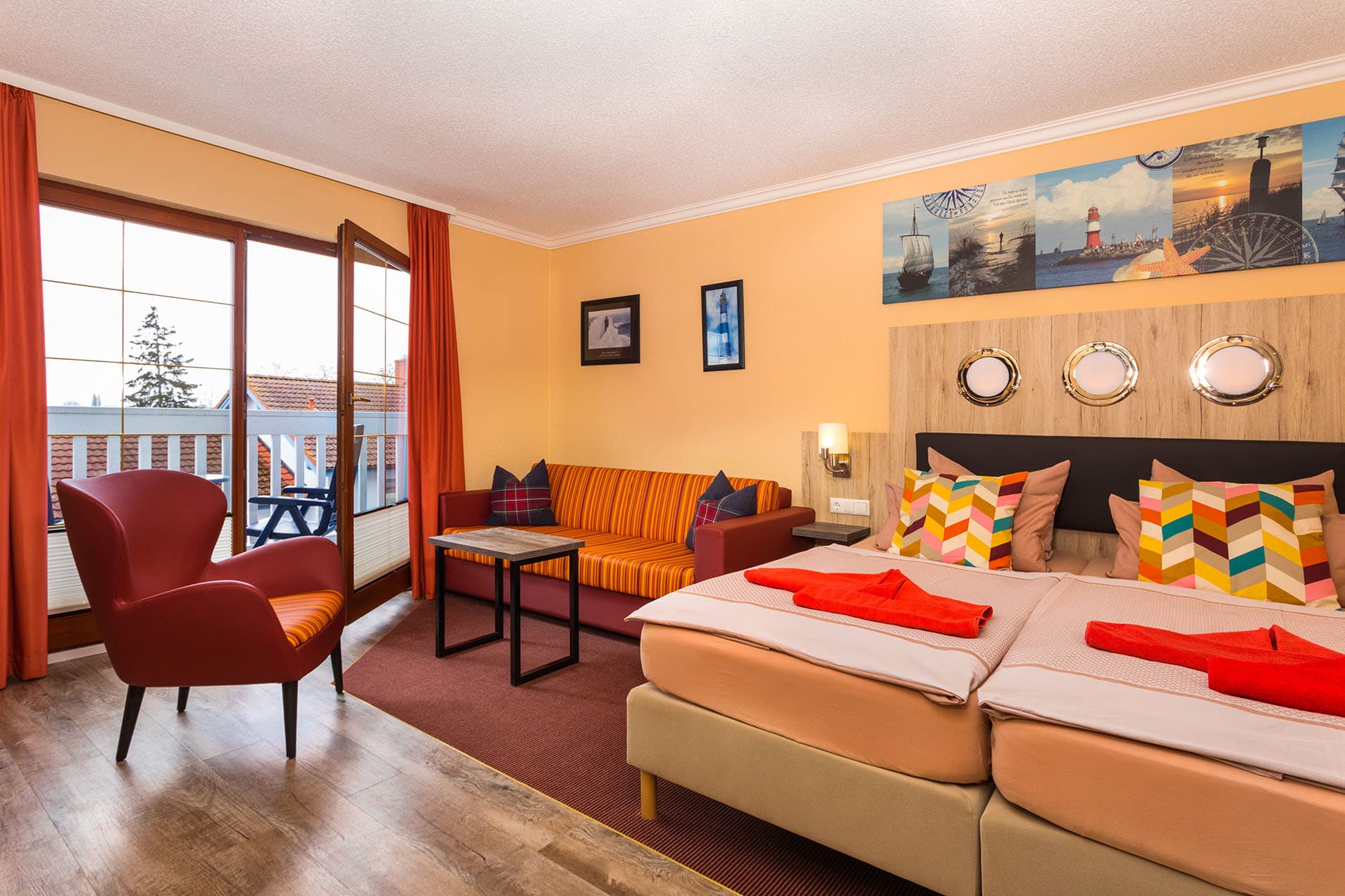 Das Bild zeigt ein helles, farbenfrohes Doppelzimmer mit großzügigem Doppebett, bewuemem Sessel und Balkon.