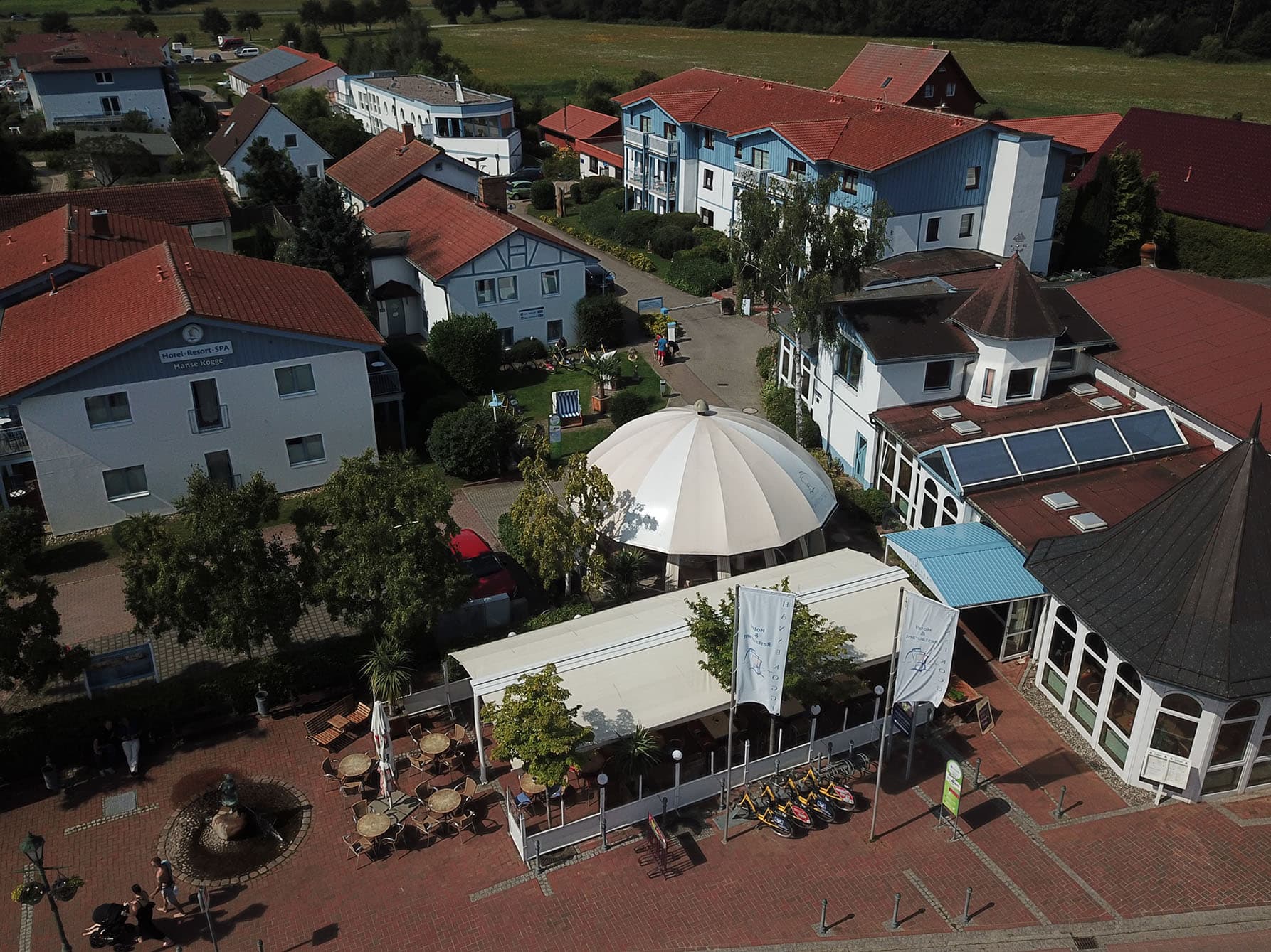Draufsicht auf die ansprechende Anlage des Hotel und Restaurant Hanse Kogge mit überdachter Außenterrasse, Veranstaltungspavillon und verschiedenen Gebäuden zur Übernachtung