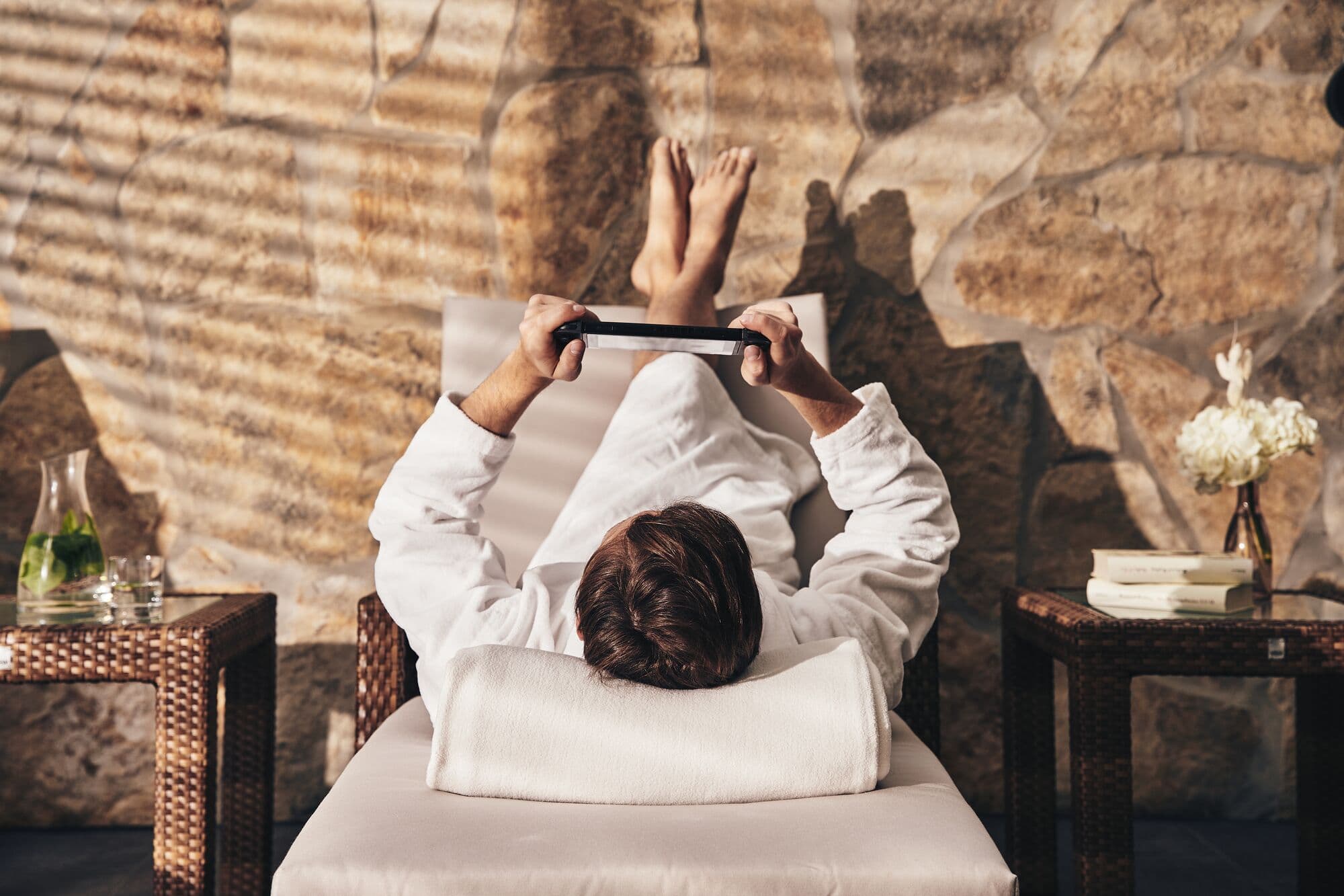 Mann entspannt mit Tablet oder E-Redaer auf Liege im Wellnessbereich