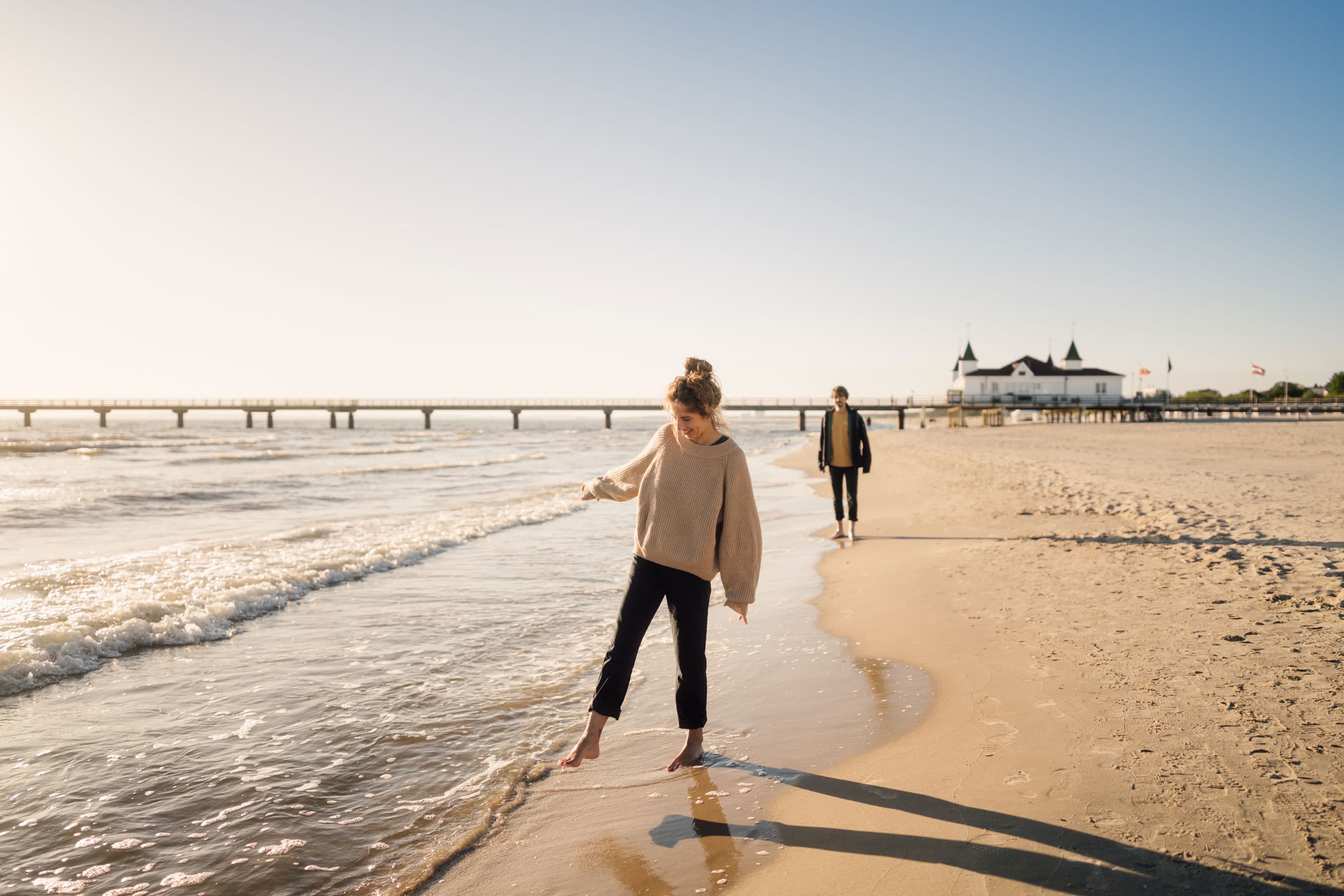 Ein Parr spaziert entlang des Strandes in Ahlbeck. Im Hintergrund ist die Ahlbecker Seebrücke zu sehen.