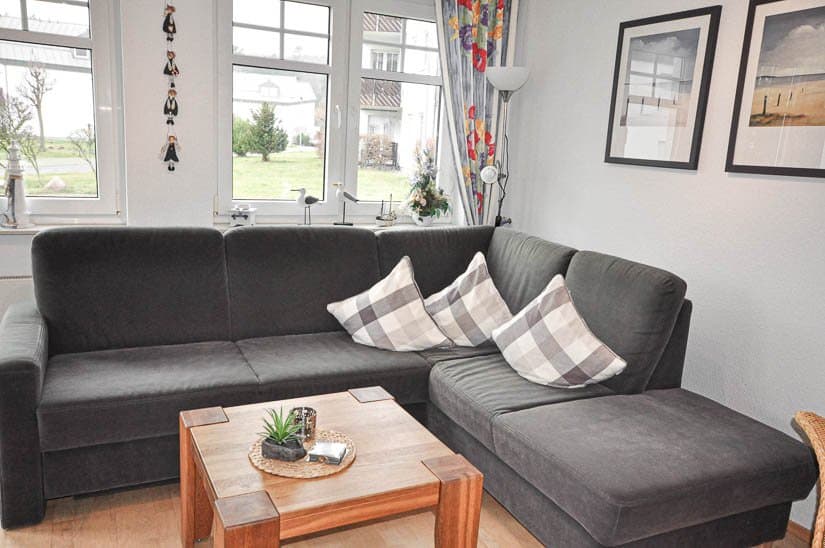 graue Couch aus Stoff mit stilvollen Kissen und einem kleinen hölzernen Beistelltisch, vor einem Panoramafenster