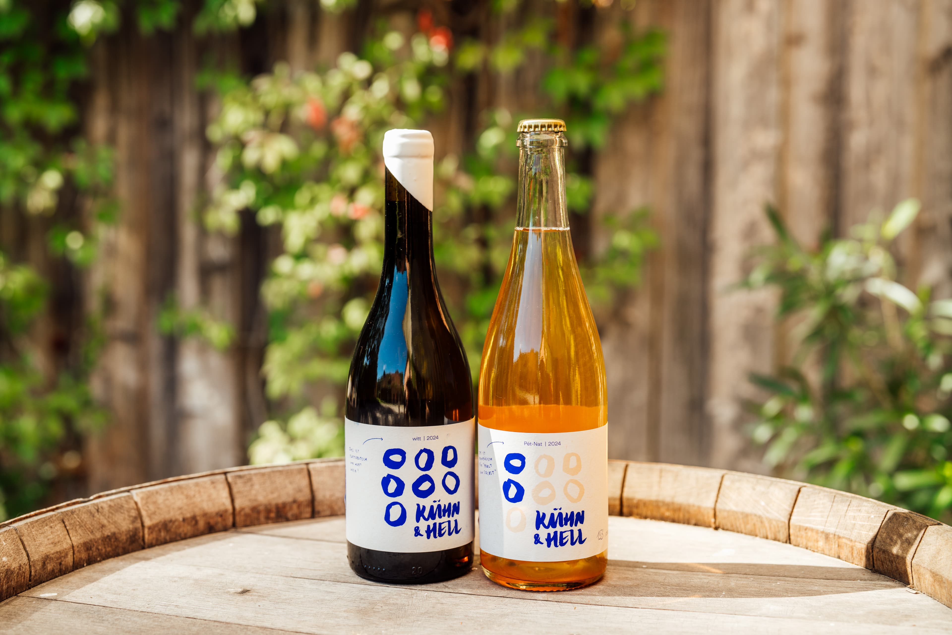 zwei Weinflaschen auf einem Fass vor sommerlicher Kulisse