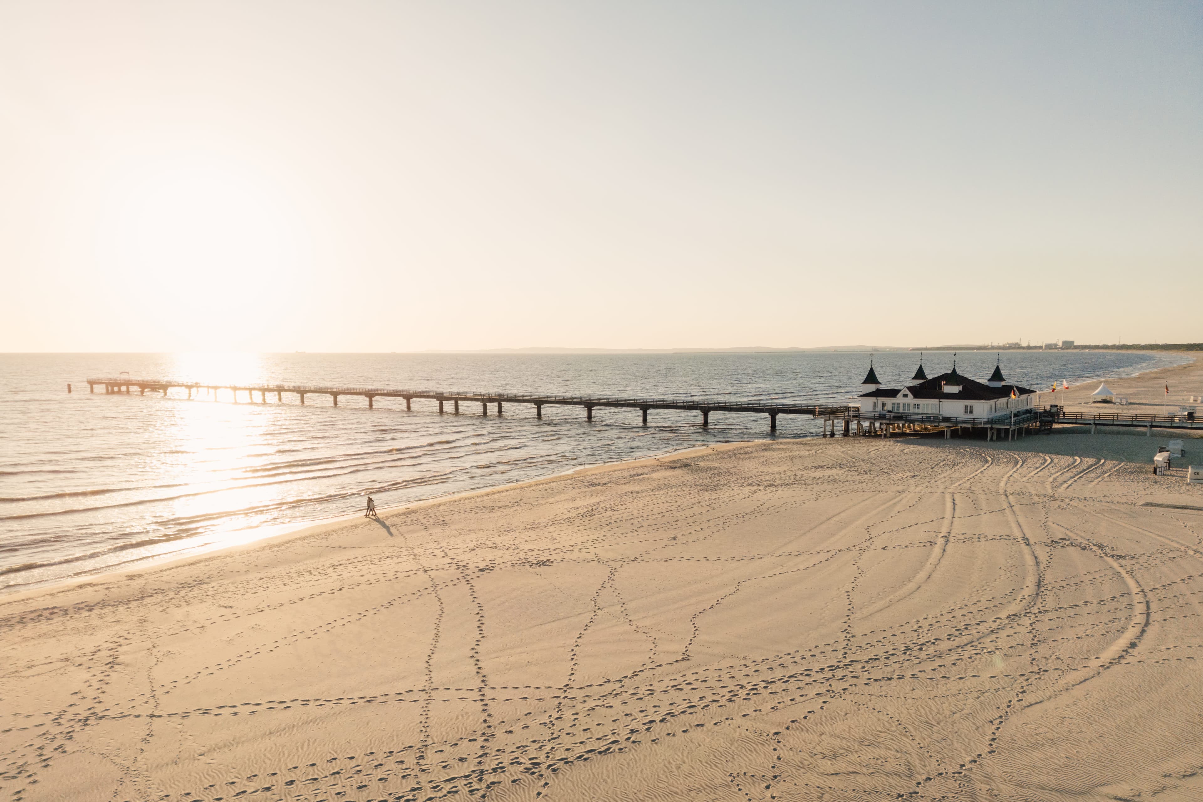 Paar spaziert am Strand von Ahlbeck zum Sonnenaufgang mit Seebrücke im Hintergrund aus der Luft_0